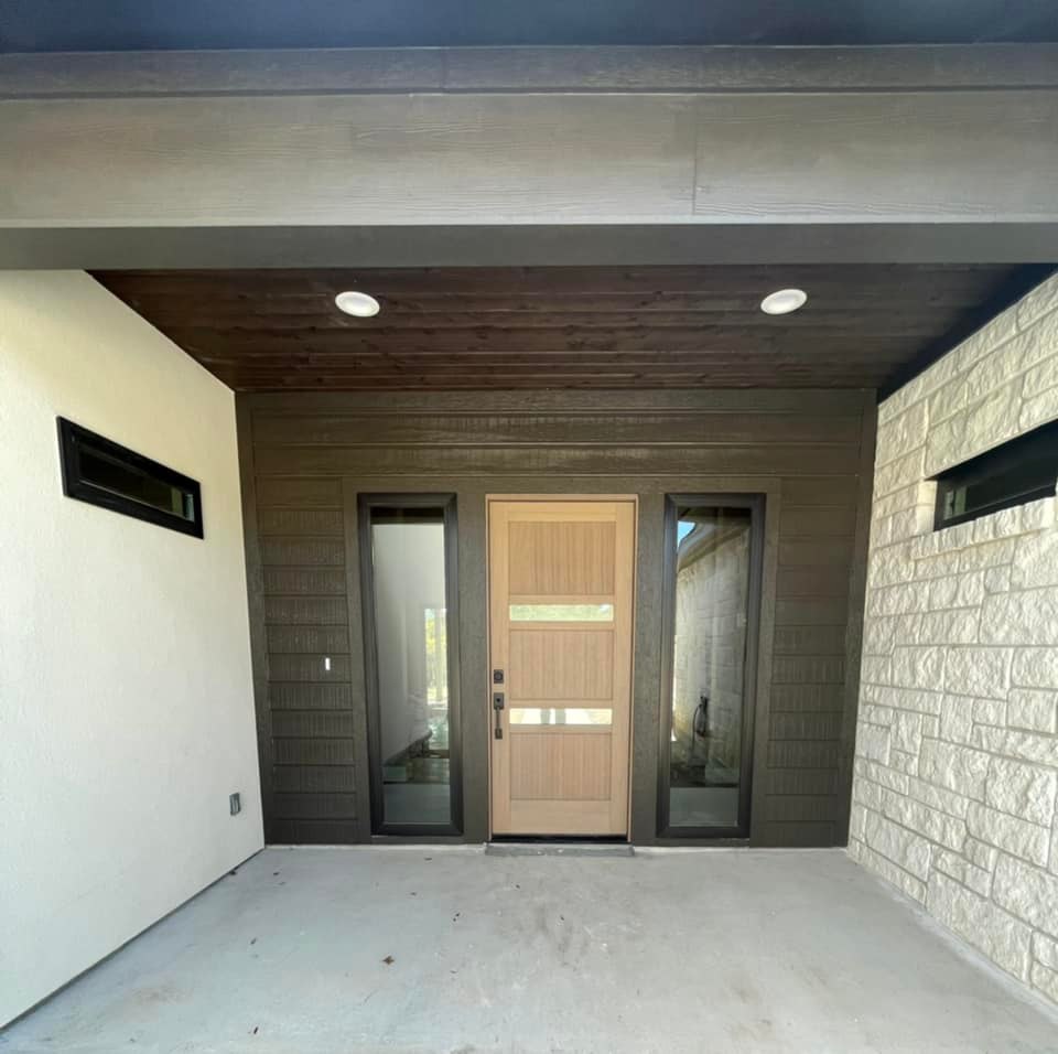 A welcoming entryway of a modern home featuring a wood-accented ceiling and a sleek door, blending contemporary and natural elements effectively.