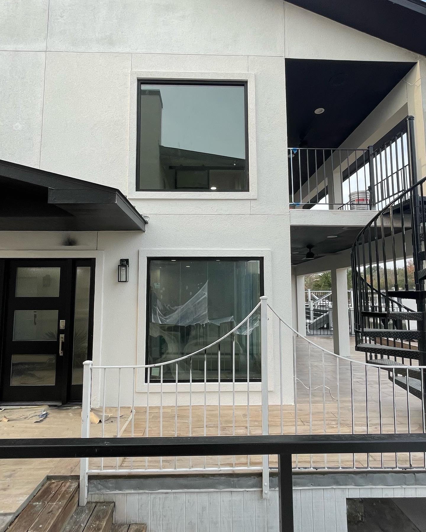 A modern home's outdoor space featuring a black spiral staircase, balconies with clean white railings, and a ground floor patio area, all designed with contemporary aesthetics.