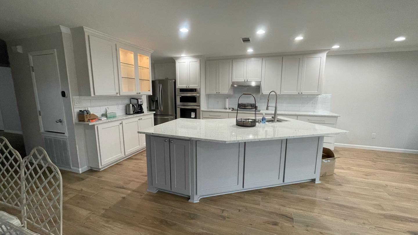 A newly remodeled kitchen featuring white cabinetry, stainless steel appliances, and a large center island with a gray base and white countertop.