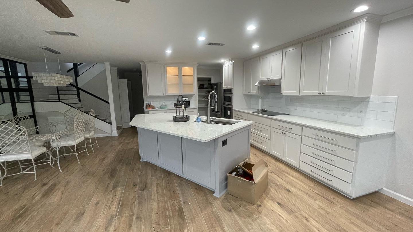 Interior view of a modern kitchen with white cabinetry, a large central island with gray base and white countertop, surrounded by a dining area with stylish black and white chairs.