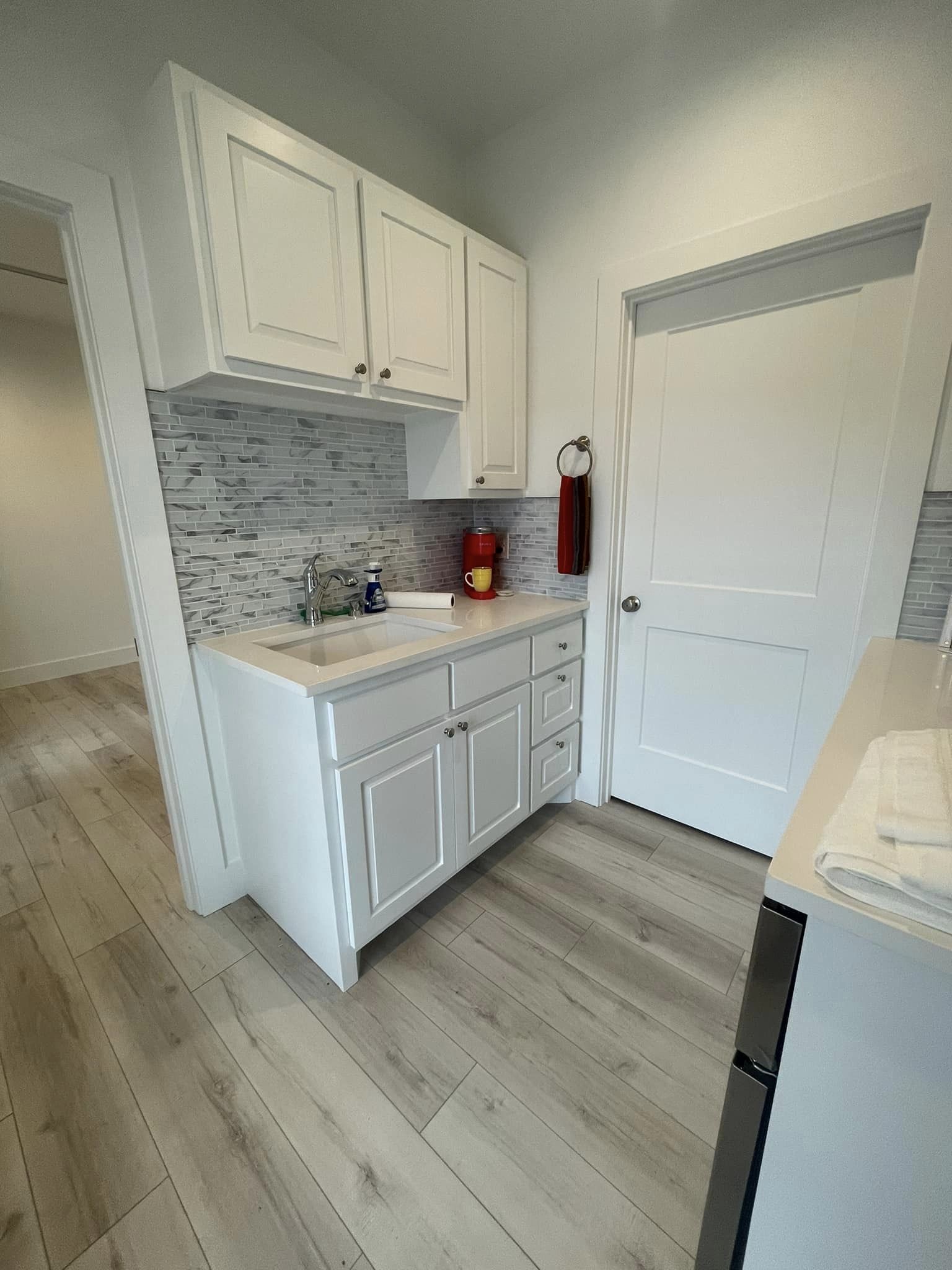 A small kitchenette with white cabinets, a gray backsplash, and modern appliances, efficiently designed to maximize space and functionality.