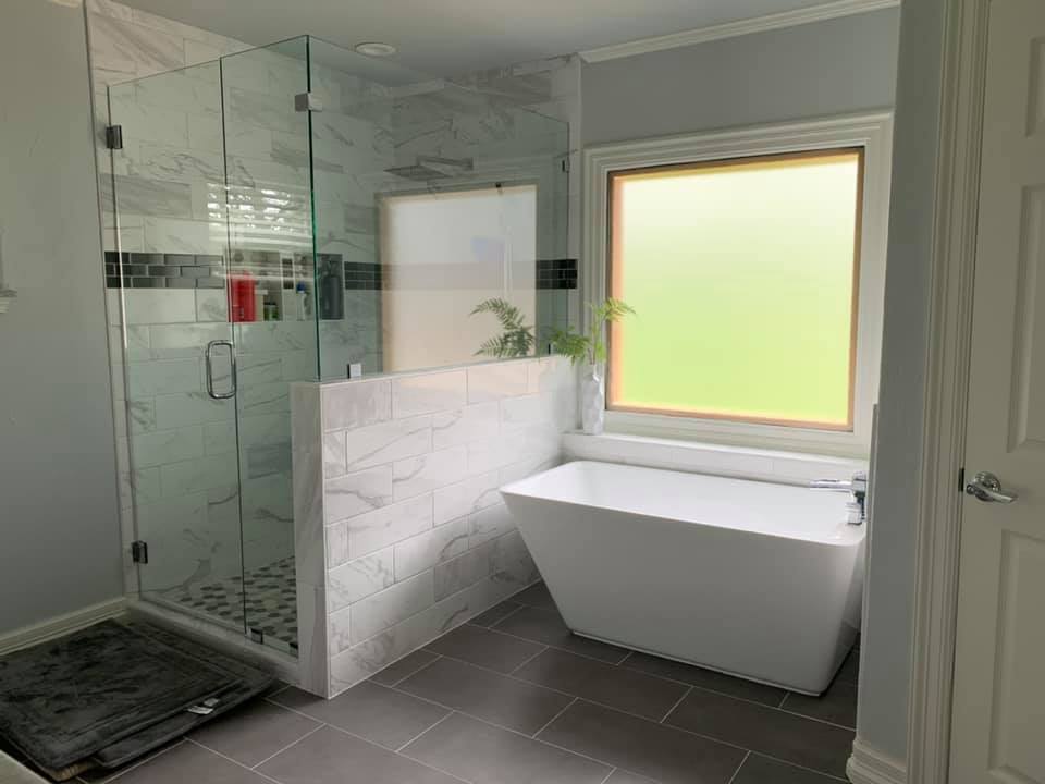 A spacious bathroom showcasing large marble tiles, a freestanding tub, and a glass-enclosed shower with detailed tile work and modern fixtures.