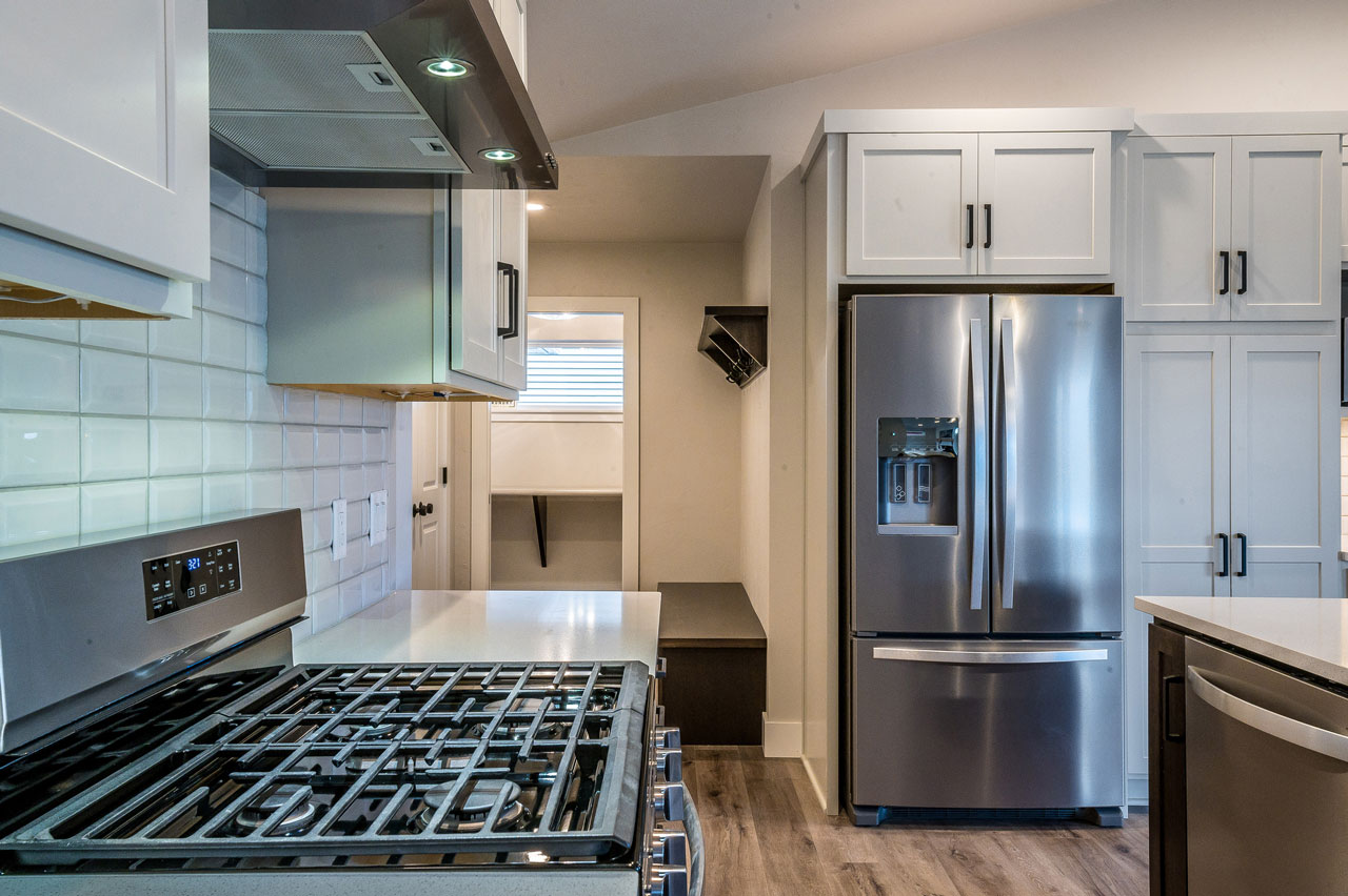 A compact and efficient modern kitchen with stainless steel appliances, white subway tiles, and light gray cabinetry.